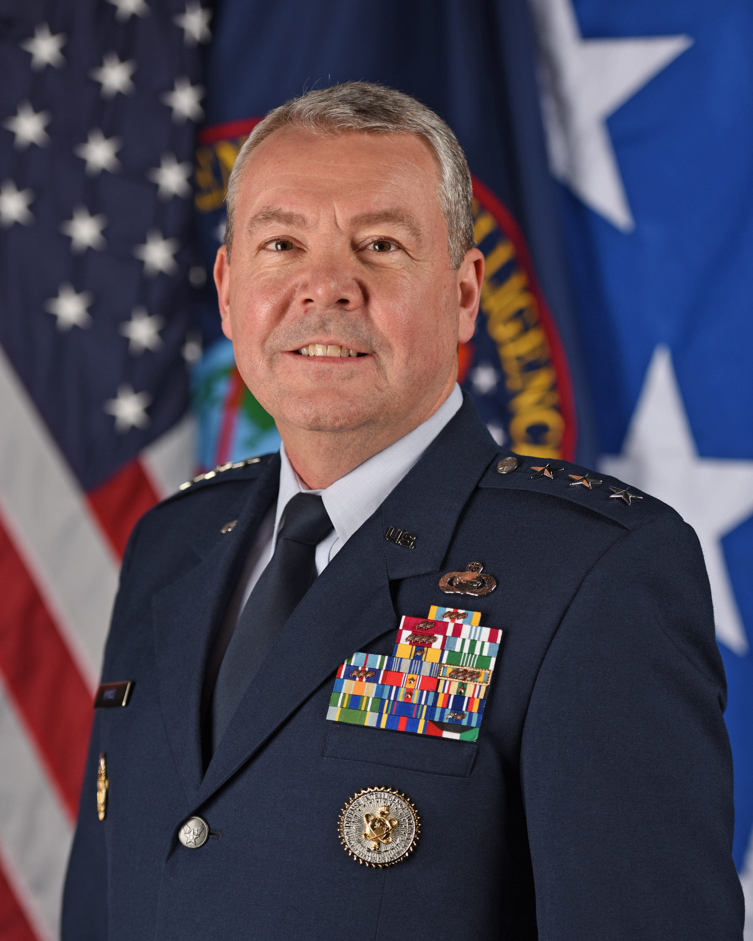 Picture of a decorated, military man in front of flags