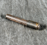 A small, cylindrical metal pin with some rust and corrosion, lying on a dark fabric background.