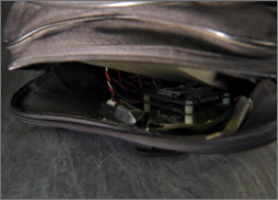 A partially opened side compartment of the duffel bag reveals a hidden electronic device with circuit boards and wiring.
