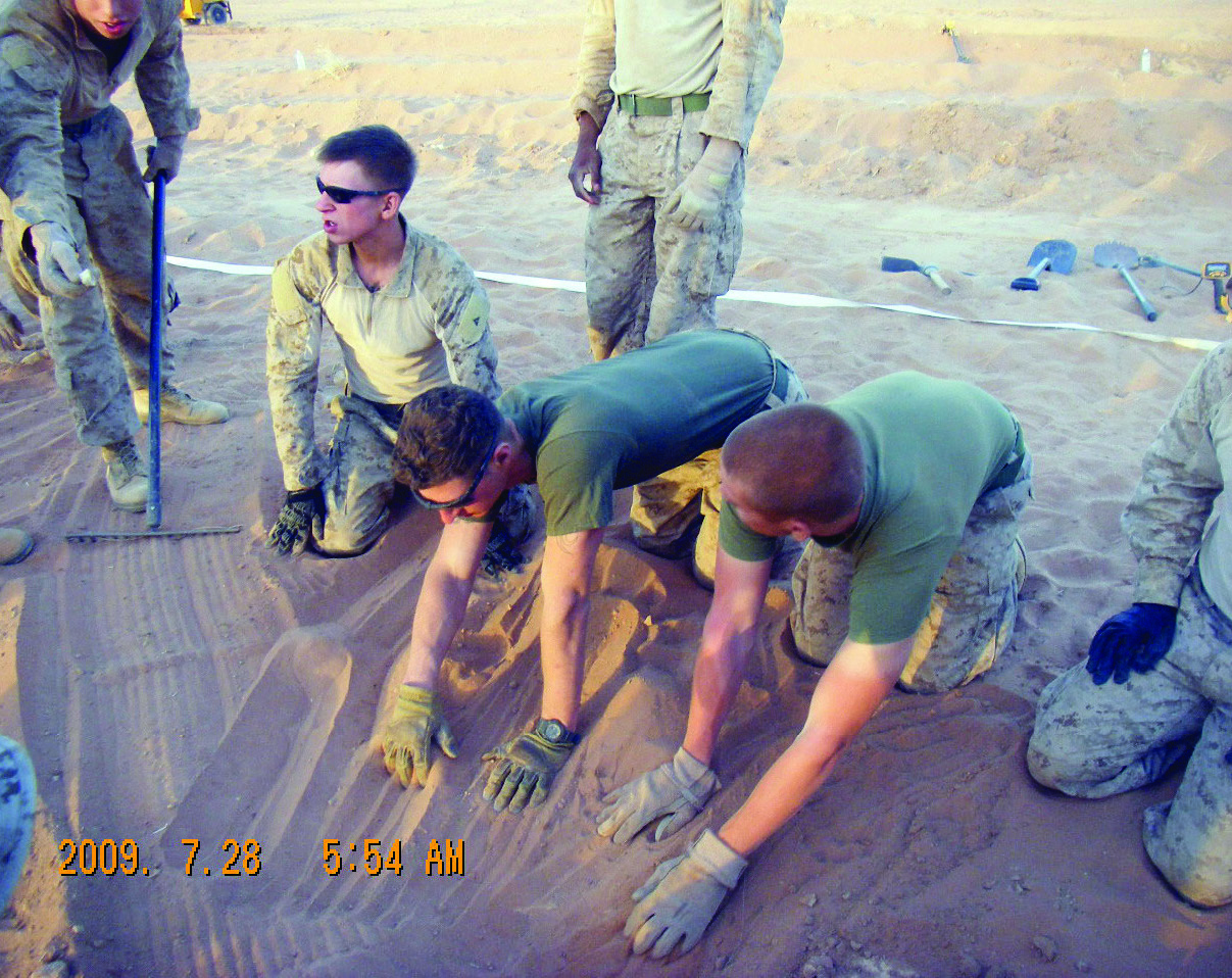 Marines conduct a meticulous search by hand, crawling and smoothing the sand in a designated lane at a recovery site, dated 28 July 2009.