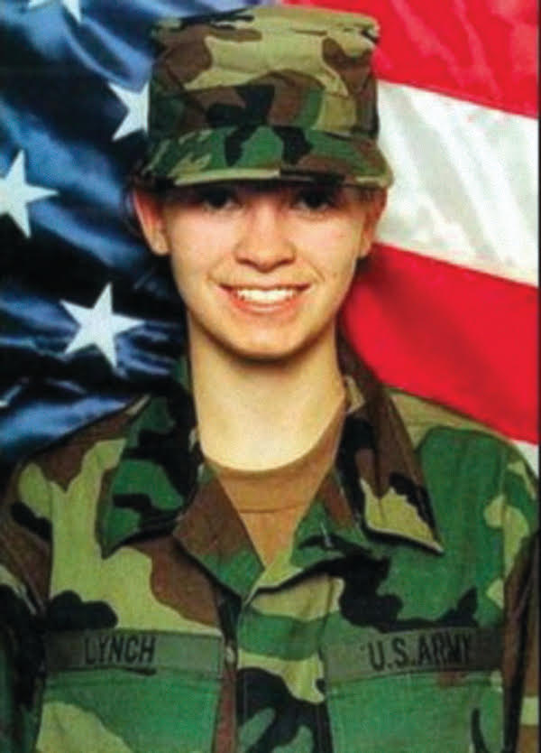 A portrait of a smiling Private First Class Jessica Lynch in her U.S. Army combat uniform, posing in front of an American flag.