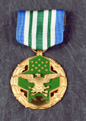 The Joint Service Commendation Medal, featuring a green and gold medallion with an eagle and stars, suspended from a blue, white, and green striped ribbon.