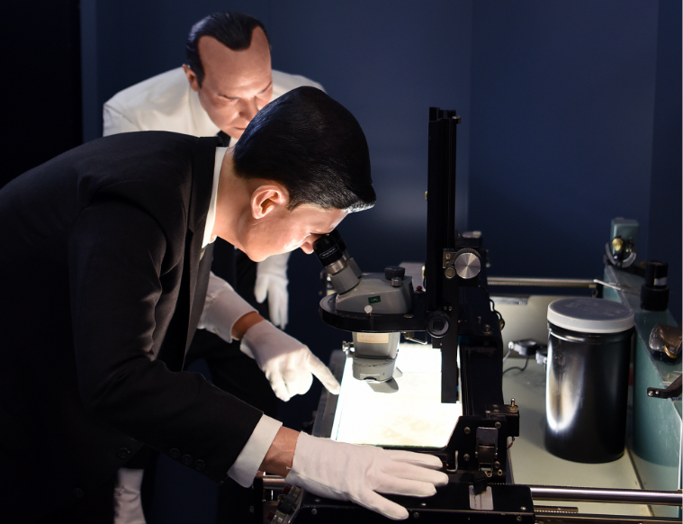 Image of a wax figures leaned over a light table