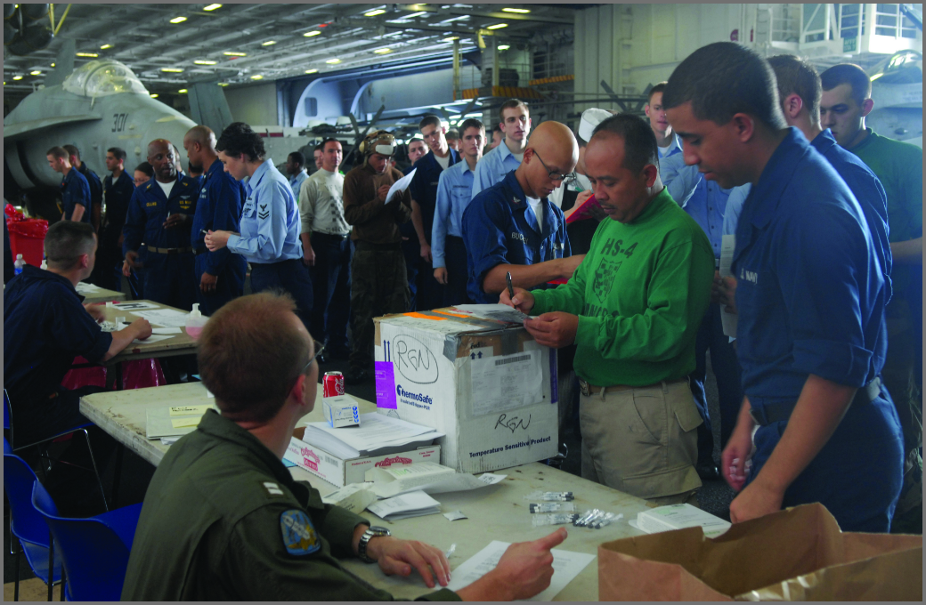 Image of a crowd with an individual in the foreground sitting at a table, helping those closest