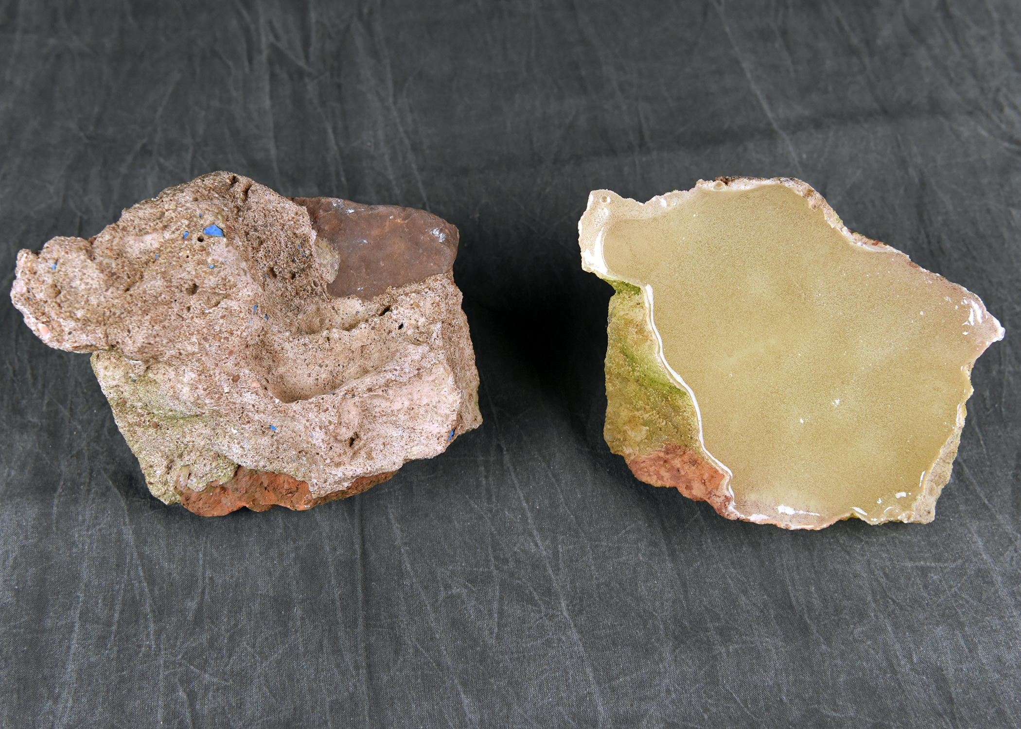 Two distinct pieces of material on a dark surface: one is a rough, reddish-brown rock, and the other is a smoother, solid yellow piece.