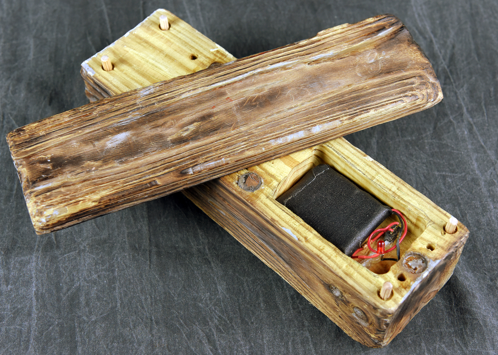 An open rectangular box with a realistic wood-grain texture. A smaller black object is visible inside the box. The lid rests partially on top.