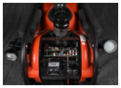 A top-down view of an orange and black remotely operated vehicle (ROV). The clear rear panel reveals the internal electronic components, and two external lights are visible on either side.