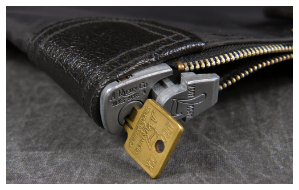 A close-up of a metal lock and key securing the zipper of a black leather bag or pouch.