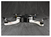 A quadcopter drone, with a black central body and white arms, is shown resting on a dark, rumpled fabric background.