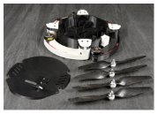 A disassembled quadcopter drone with its components laid out on a dark, rumpled fabric. The parts displayed include the main body with folded arms, four separate propellers, and the top cover plate.