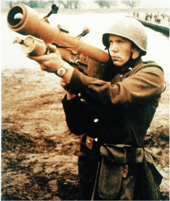 A soldier in a helmet and uniform aims a shoulder-fired missile launcher.