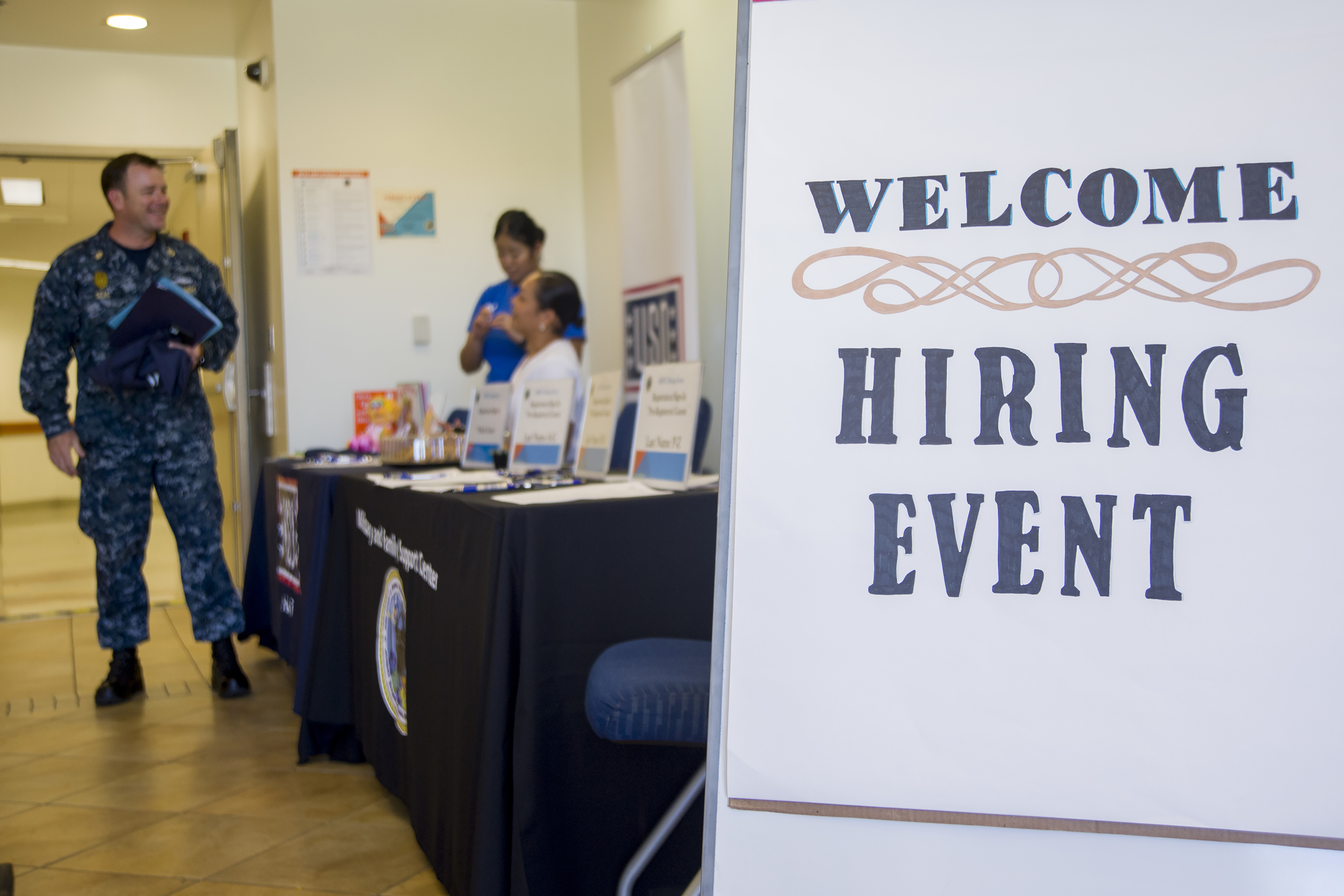 Image of uniformed member at hiring event welcome table. With two people are behind the table.